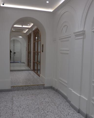 Enfilade d'arches, panneaux moulurés blancs, granito moucheté et porte vitrée en bois au fond