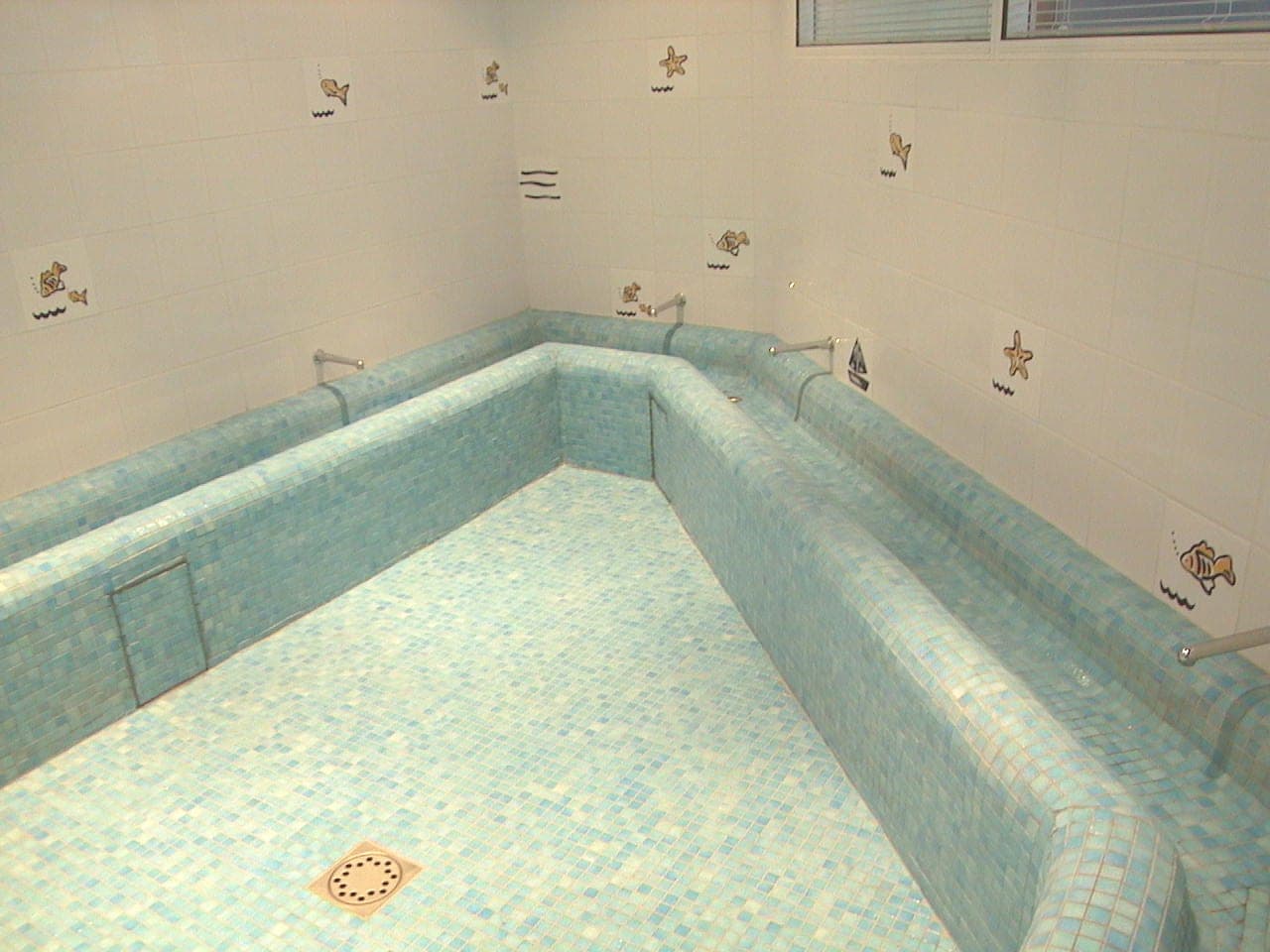 Bassin carrelé en mosaïque turquoise, margelles et marches, faïence blanche décorée de petits animaux
