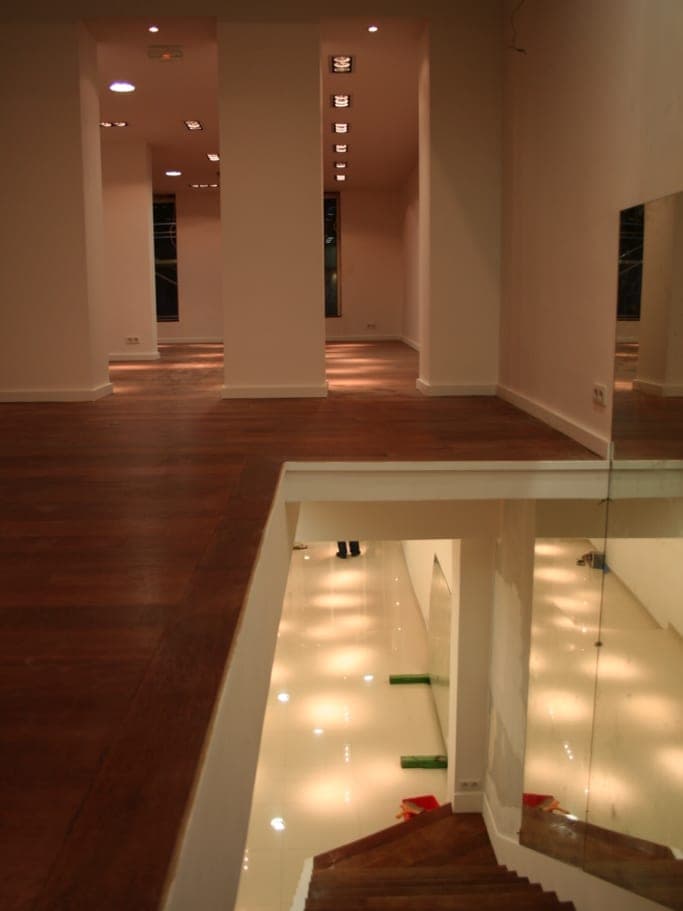 Vue plongeante depuis une mezzanine vers un escalier en bois, parquet foncé et spots encastrés