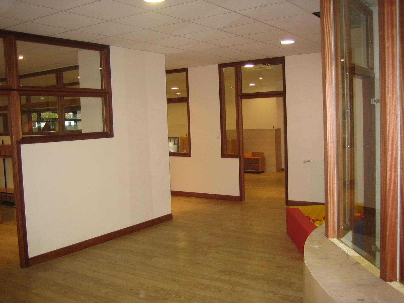Salle aux cloisons vitrées encadrées de bois, sol clair, faux plafond à spots et banquette orange