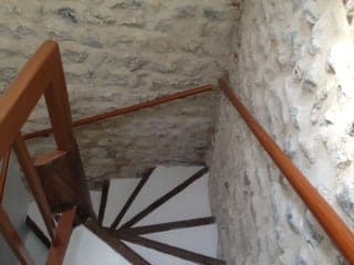 Vue plongeante sur un escalier tournant à marches blanches, entre des murs de moellons et de silex apparents