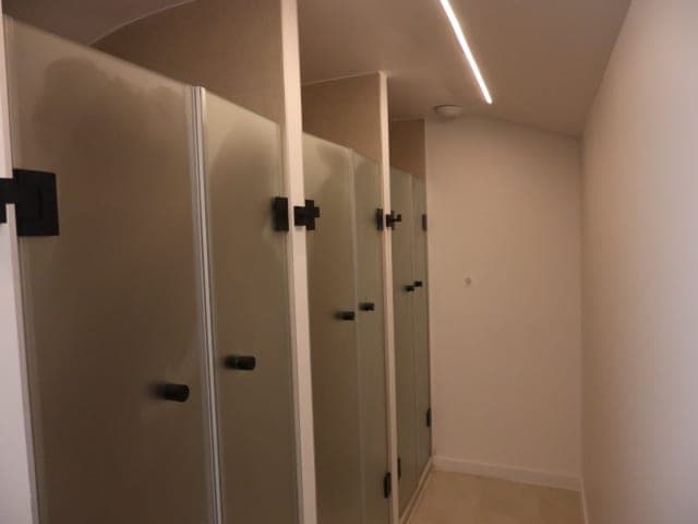 Rangée de cabines de douche en verre dépoli à poignées noires, ligne lumineuse en diagonale au plafond