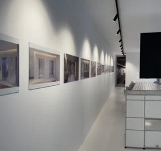Couloir blanc : cadres photo alignés sous des spots sur rail noir et meuble modulaire métallique