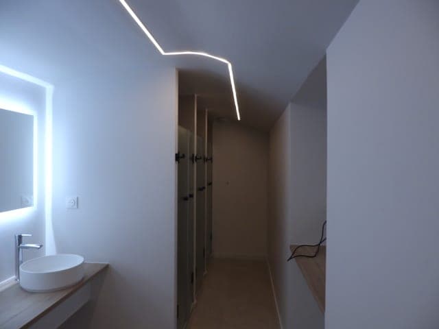 Vasque blanche sur un plan en bois, miroir rétroéclairé et ligne lumineuse brisée au plafond