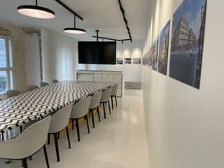Salle de réunion en longueur : table à plateau chevrons, chaises, écran mural et frise de photos d'immeubles