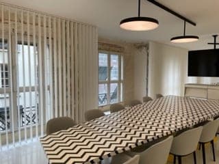 Table à plateau chevrons devant des portes-fenêtres à balcons en ferronnerie, stores à lamelles et suspensions rondes