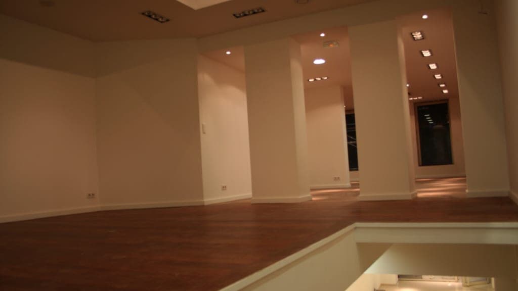Grand plateau à parquet foncé, trémie à garde-corps vitré, piliers blancs et spots encastrés