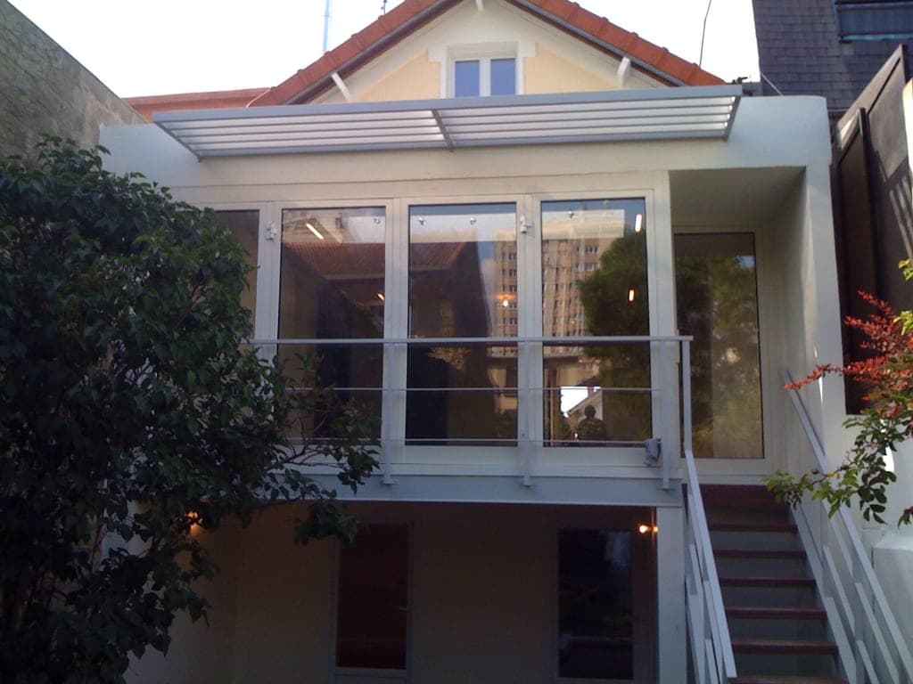 Façade arrière d'une maison : pièce vitrée à brise-soleil à lames, escalier extérieur blanc et jardin