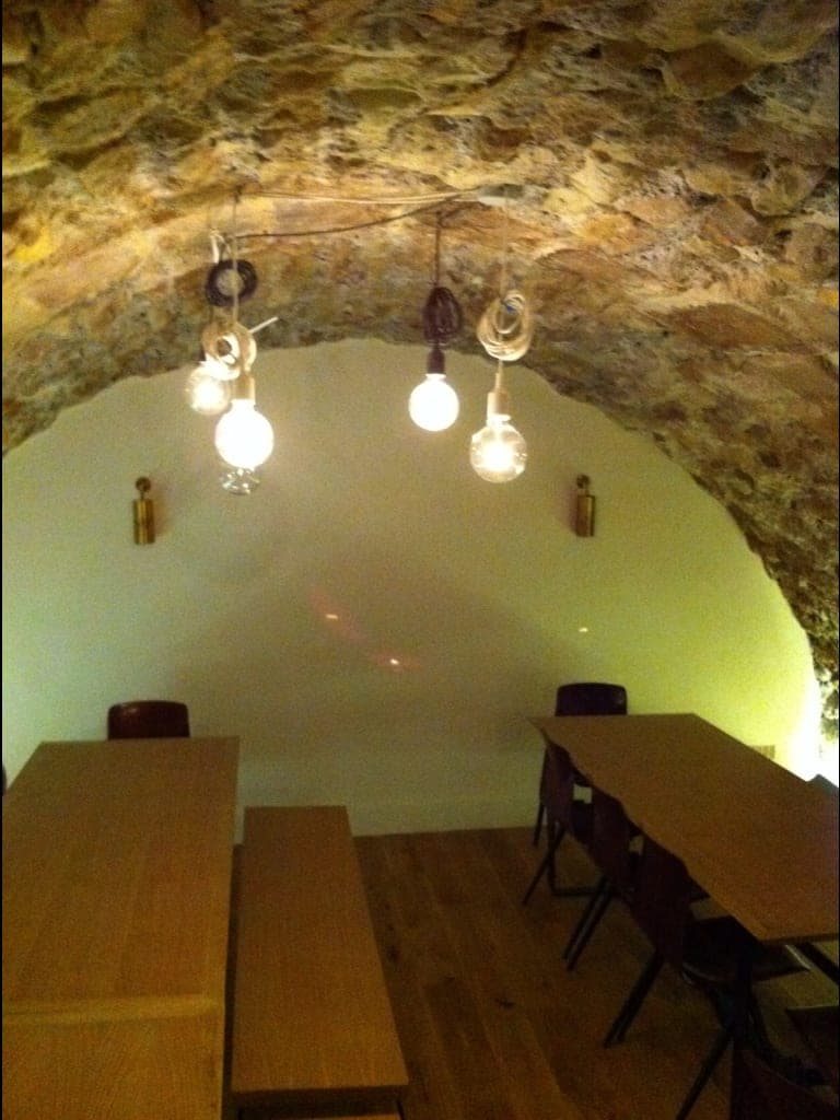 Cave voûtée en pierre : ampoules nues suspendues, tables et bancs en bois