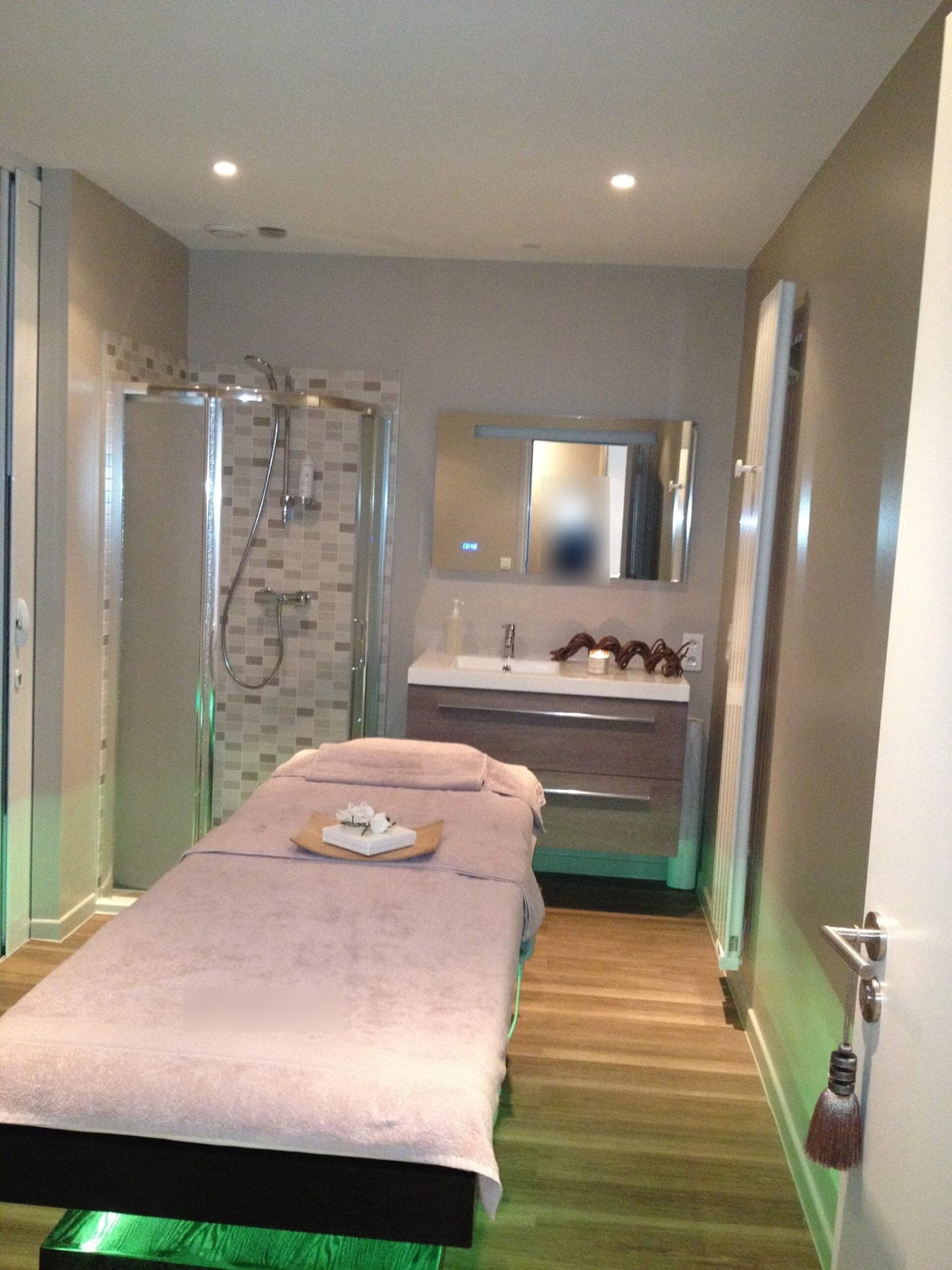Cabine de soins : table de massage, douche d'angle en mosaïque beige, meuble-vasque en bois et miroir