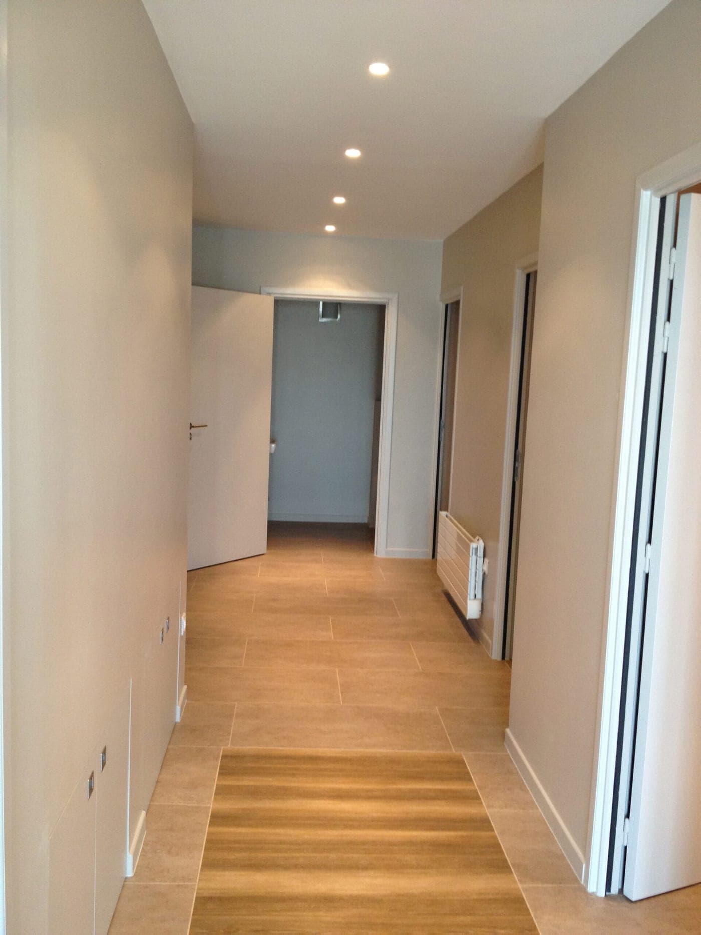 Couloir au carrelage effet bois, murs taupe, spots encastrés et porte ouverte au fond