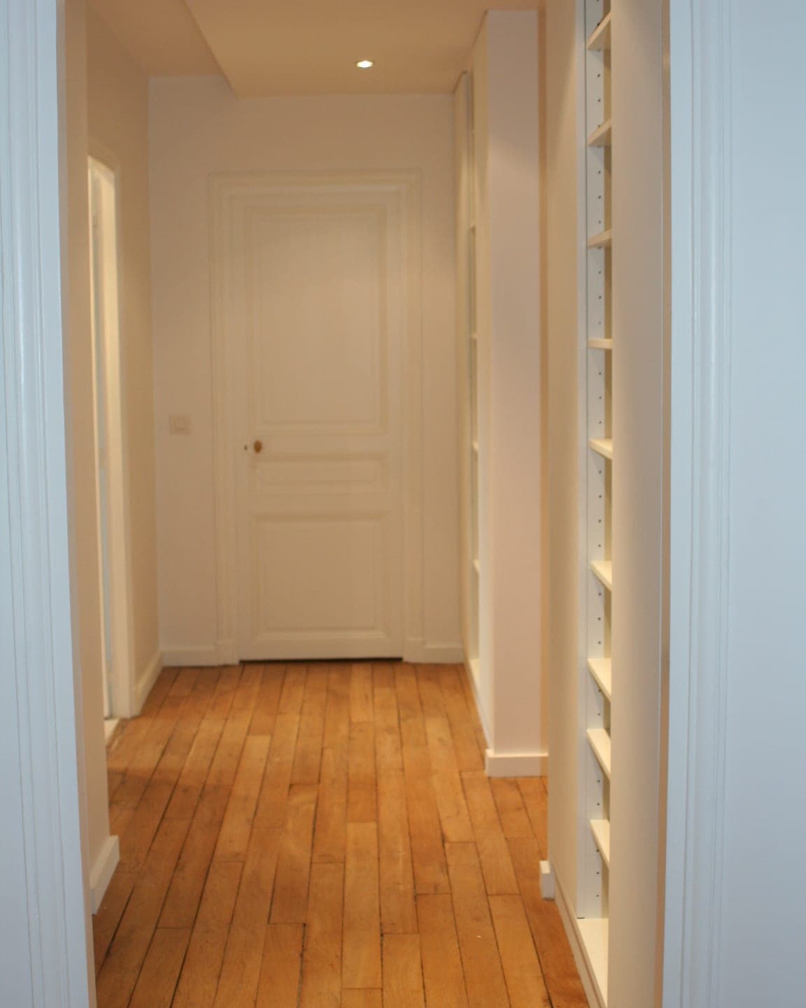 Couloir à parquet de chêne en lames, rangements encastrés éclairés et porte moulurée