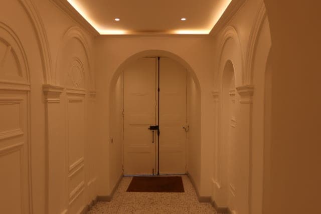 Hall en lumière chaude : arcades et panneaux moulurés peints, double porte en arc au fond