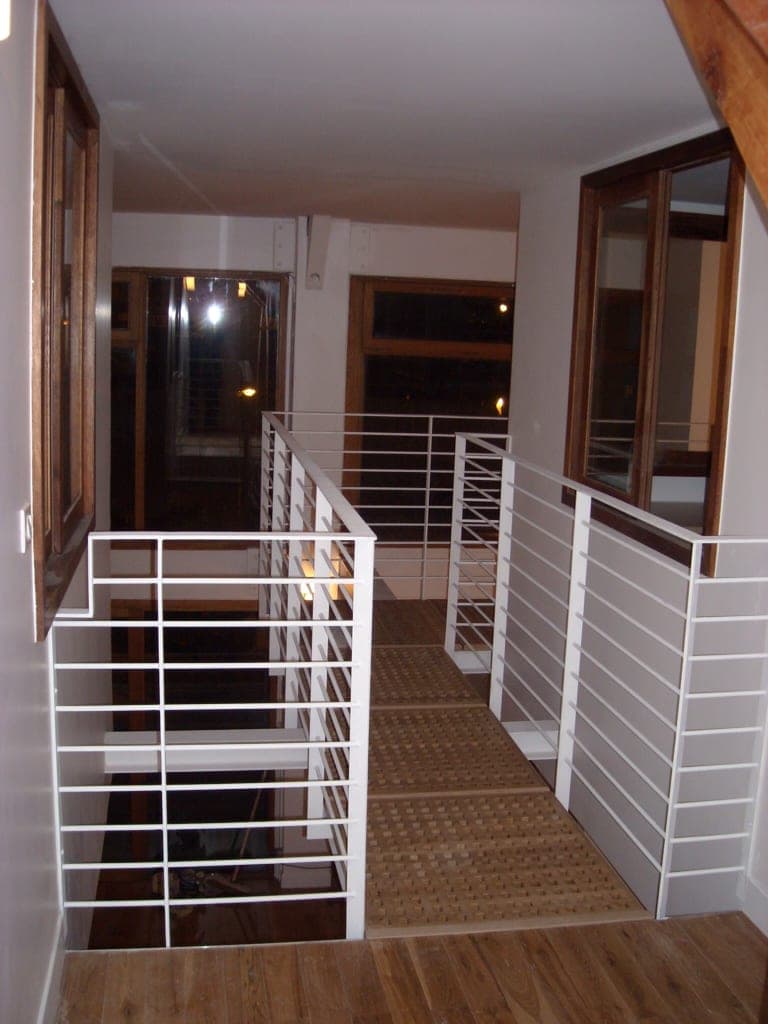 Passerelle de mezzanine à garde-corps blanc à barreaux horizontaux, sol en bois, vue de nuit