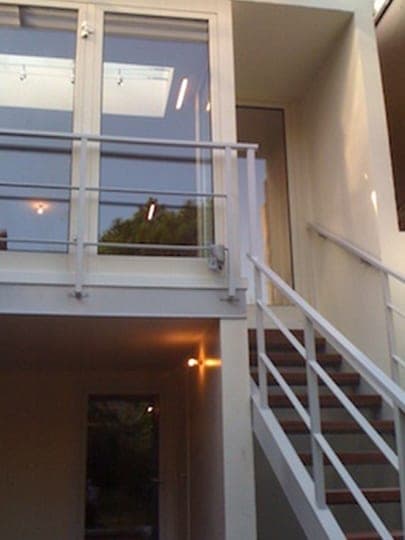 Escalier intérieur à garde-corps métallique blanc dans une double hauteur aux grandes baies vitrées