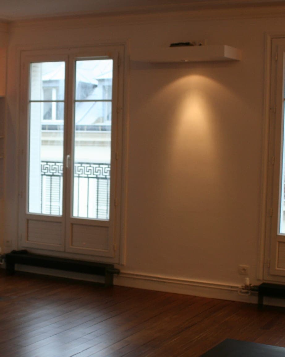 Séjour à parquet foncé : cheminée encastrée et porte-fenêtre ouvrant sur un balcon en ferronnerie