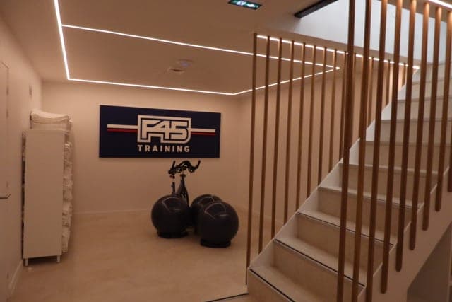 Escalier blanc à garde-corps en lames de bois, lignes lumineuses au plafond et panneau F45 Training