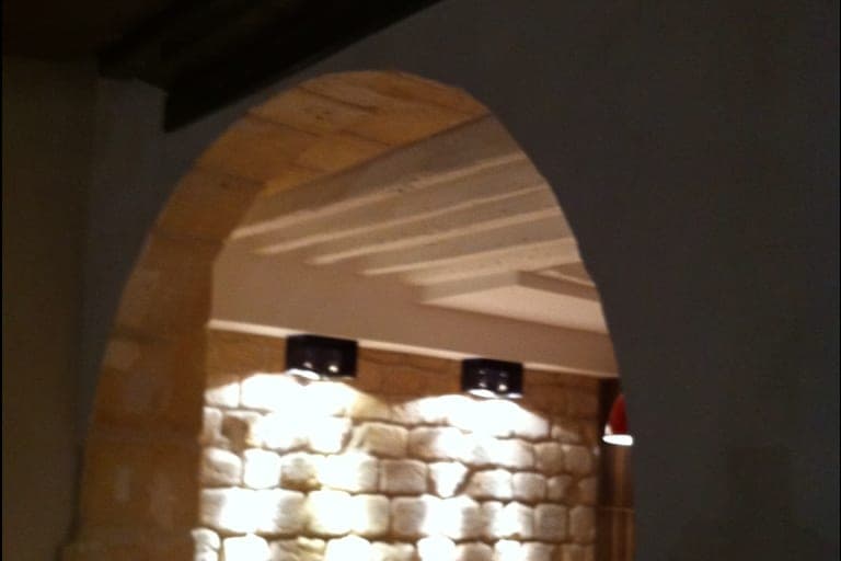 Arche en pierre de taille ouvrant sur un mur de moellons éclairé par des spots